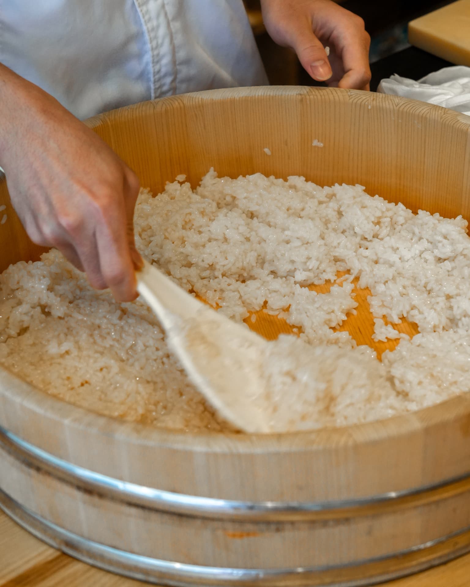 Chef folding seasoned sushi rice in a wooden hangiri